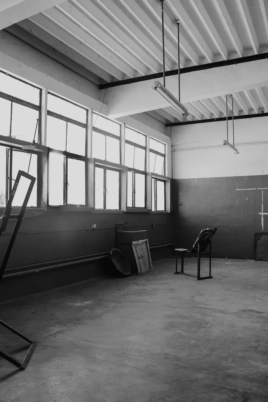 Ancien atelier industriel vide éclairé par de hautes fenêtres, en noir et blanc
