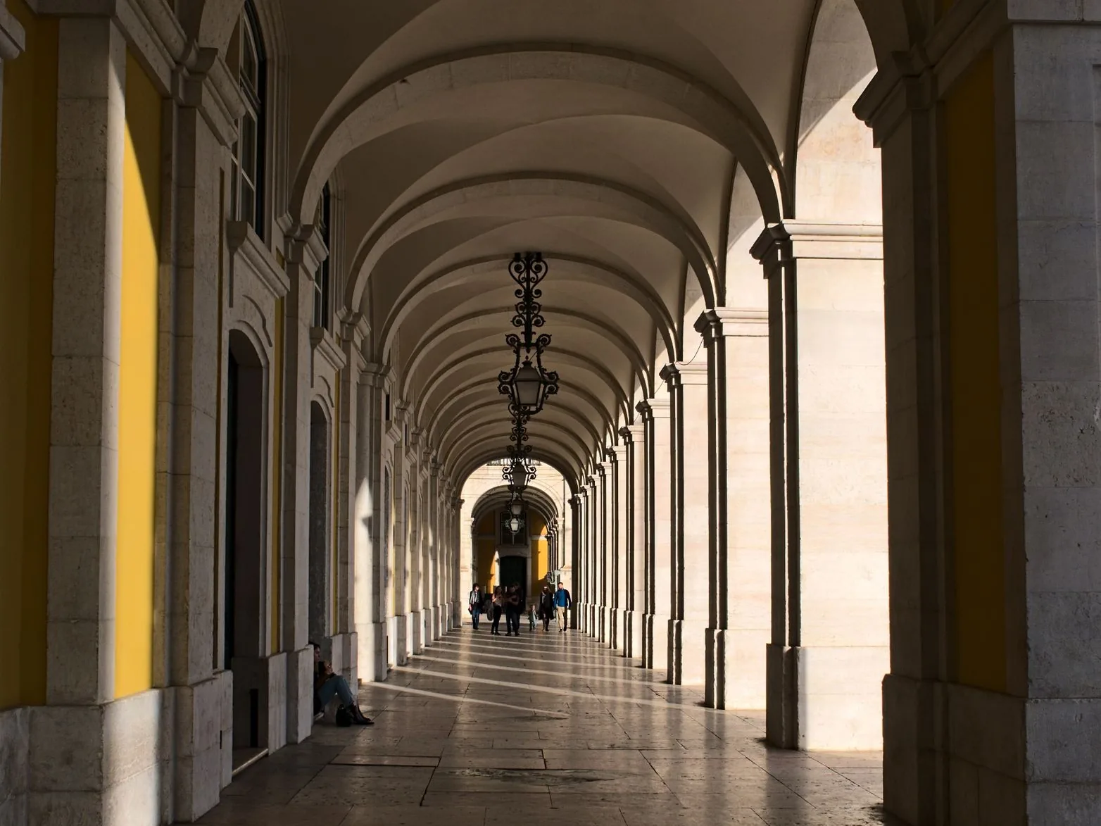 La galerie voûtée des arcades jaunes de la Praça do Comércio, à Lisbonne, avec ses lustres en fer forgé