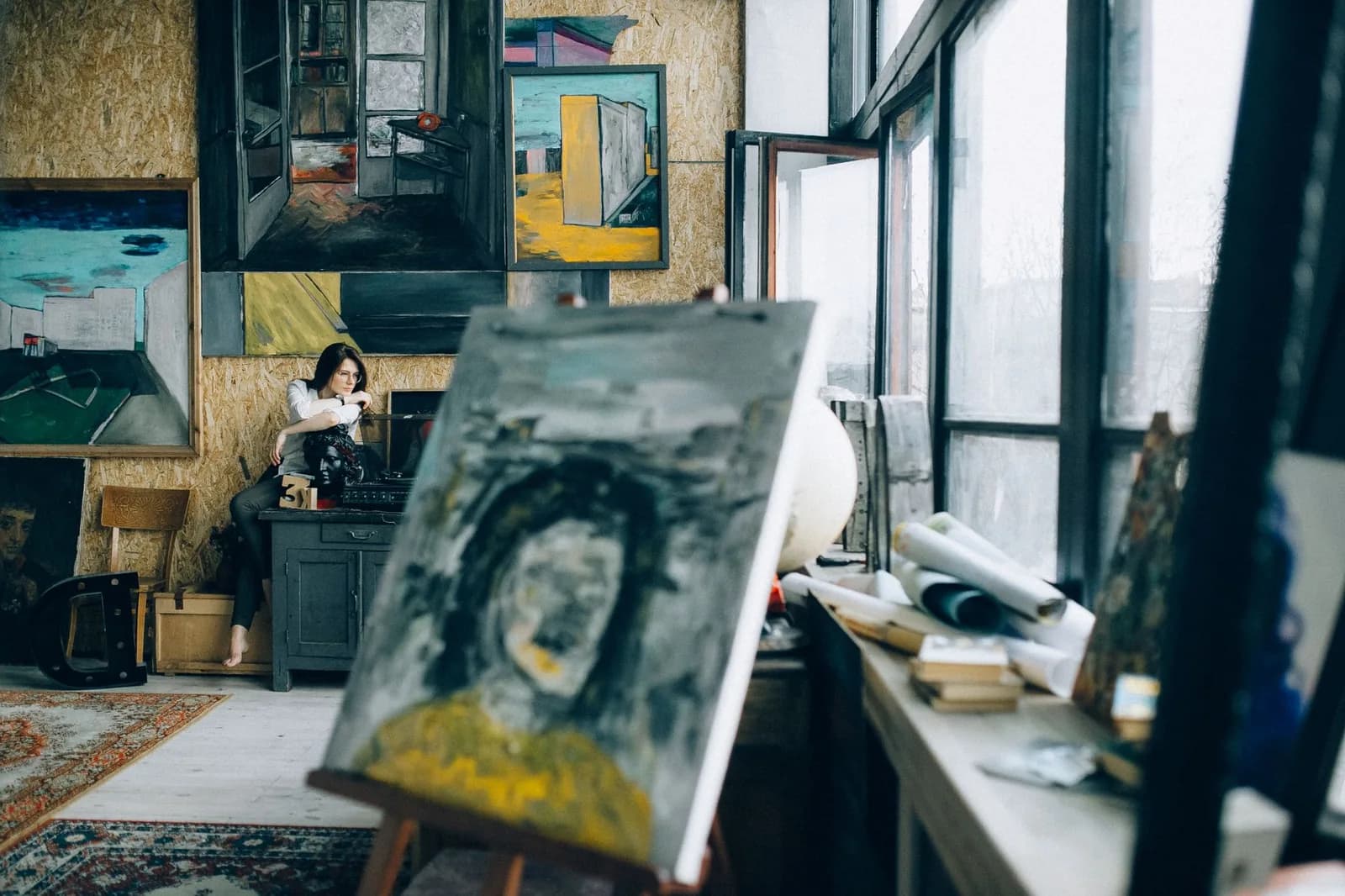 Artiste au travail dans un atelier encombré de toiles, sous une grande verrière