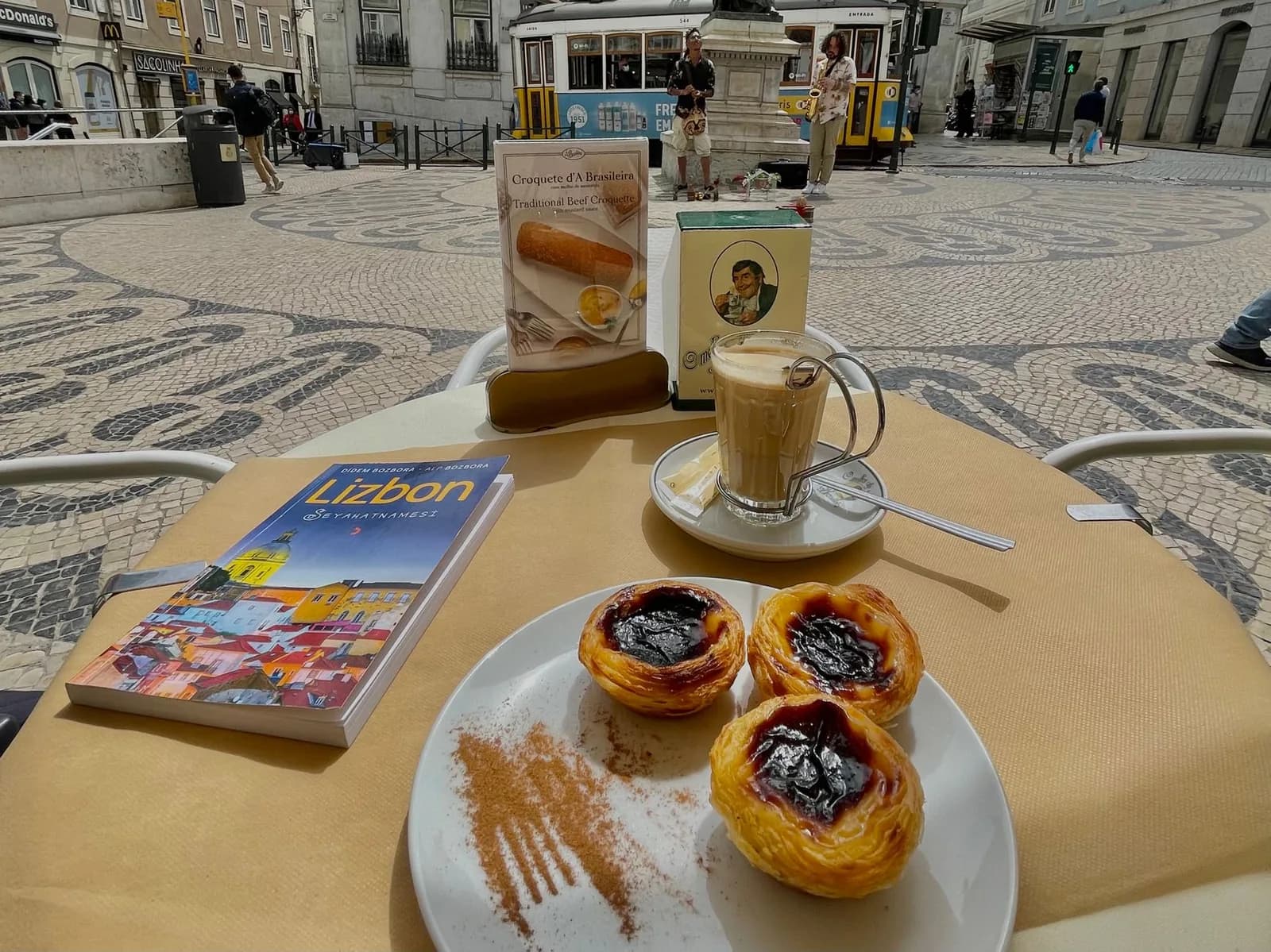Table de terrasse avec café et pastéis de nata sur une place pavée de Lisbonne, tram jaune en arrière-plan