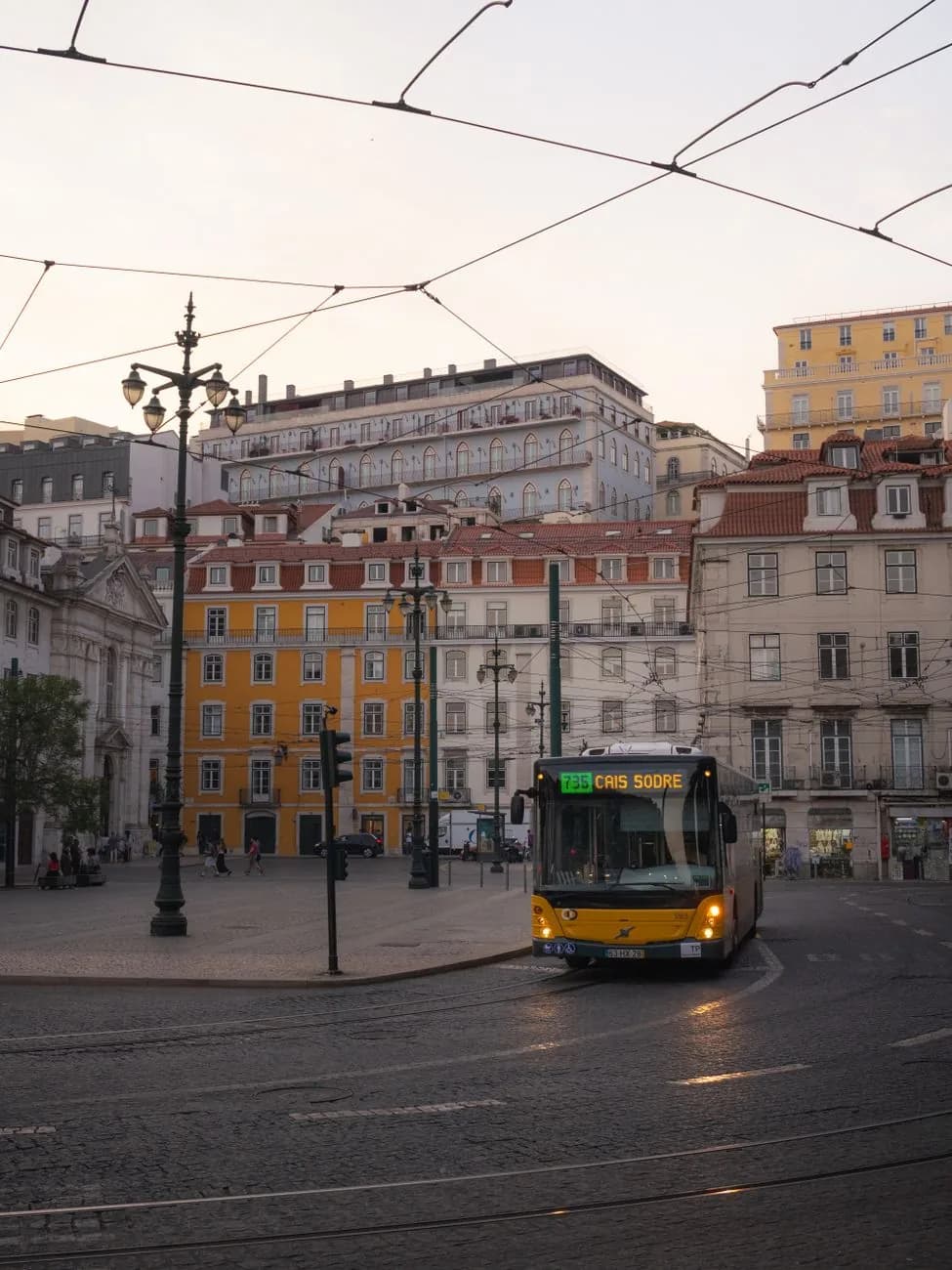 Bus urbain jaune traversant une place du centre de Lisbonne en fin de journée