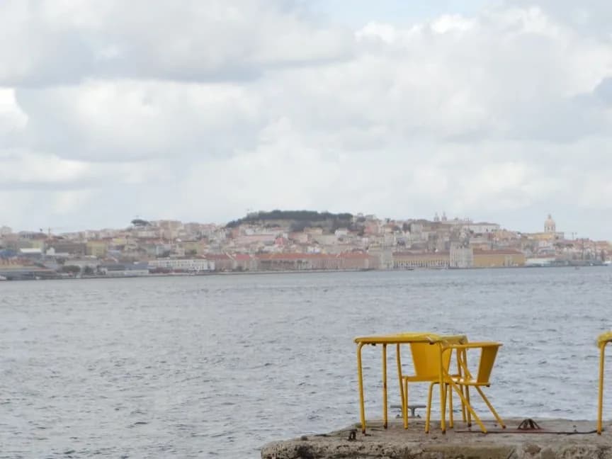 Quai en pierre au bord du Tage avec des chaises jaunes, face à la silhouette de Lisbonne