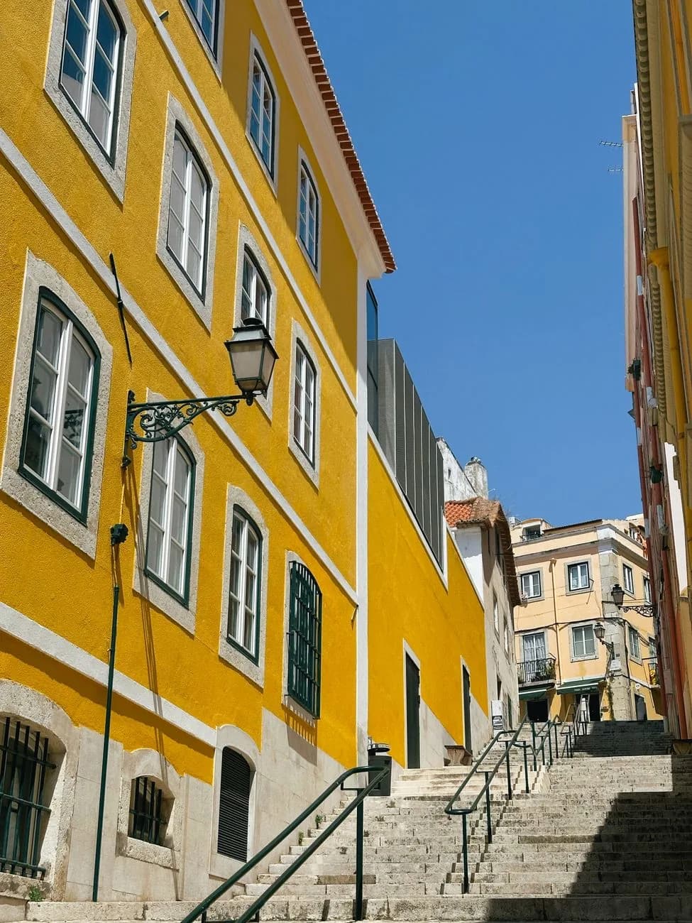 Escalier qui descend le long d'une façade jaune sous un ciel bleu, centre historique de Lisbonne