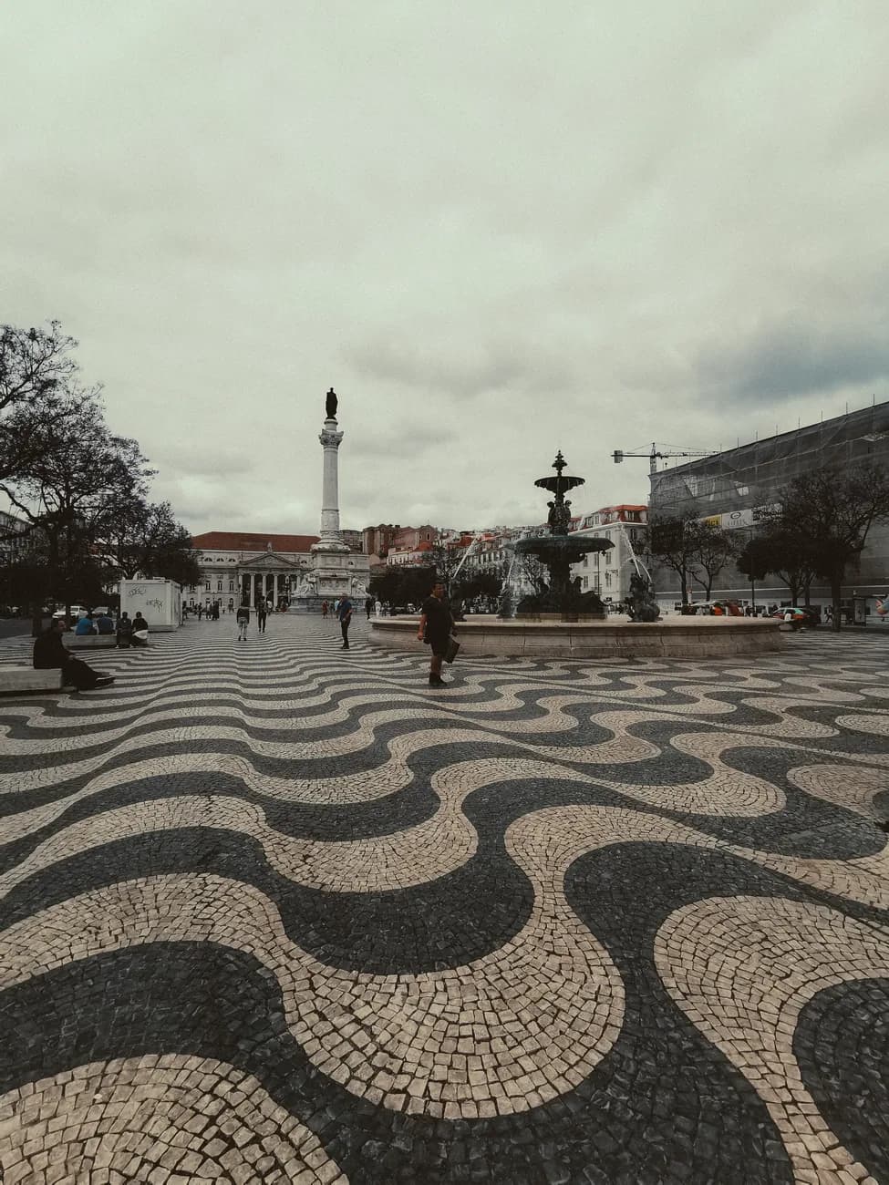 Pavage noir et blanc en vagues de la place du Rossio, avec la colonne et une fontaine au fond, Lisbonne
