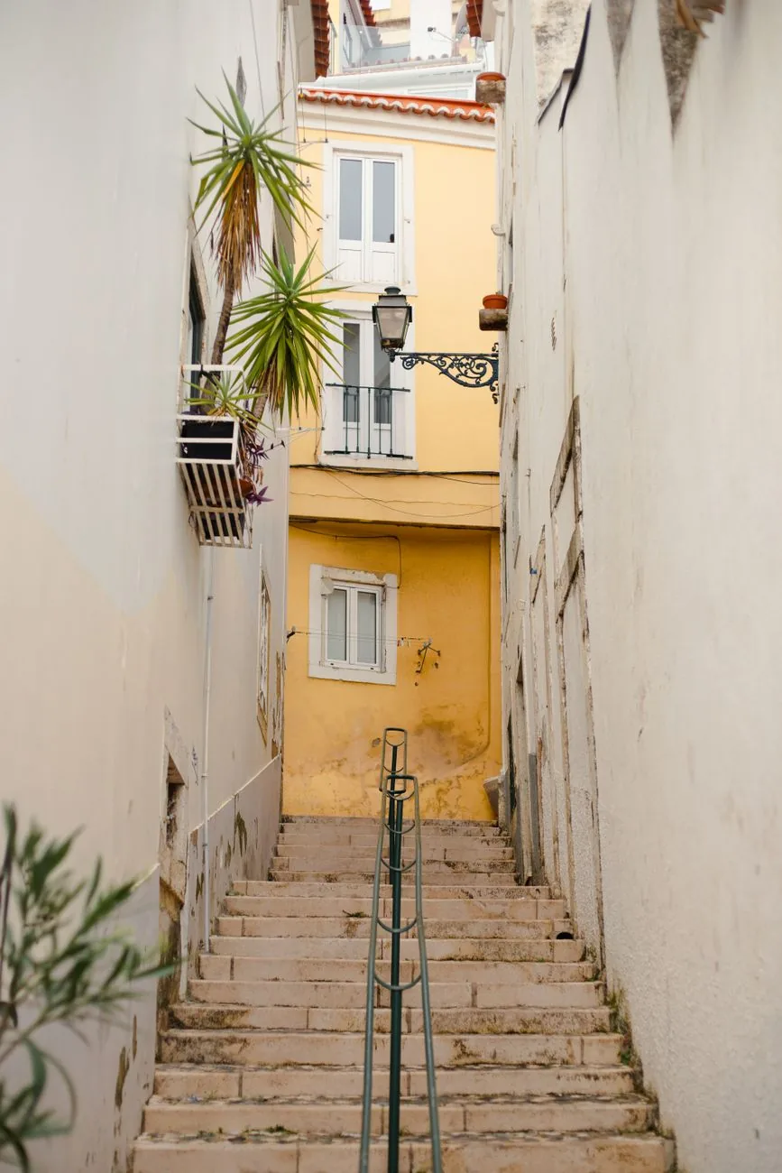 Ruelle en escaliers blancs bordée de murs chaulés, façade jaune au fond, dans l'Alfama à Lisbonne