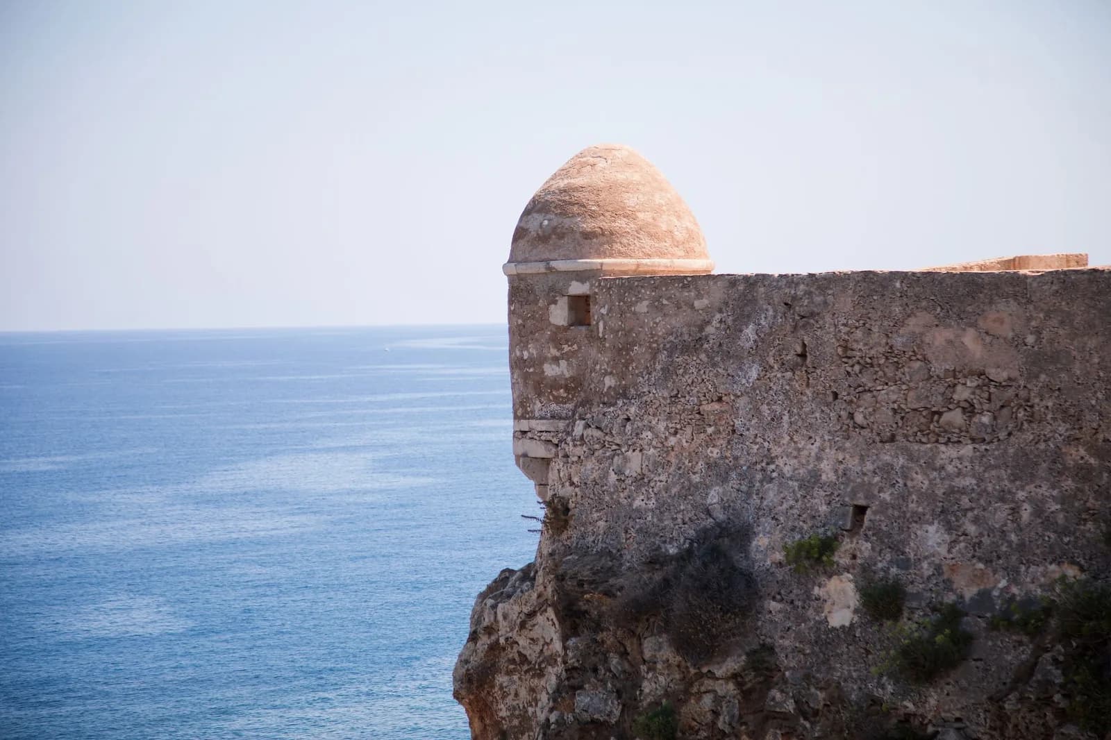 Muraille médiévale en pierre avec une échauguette en dôme, perchée sur la roche au-dessus de la mer