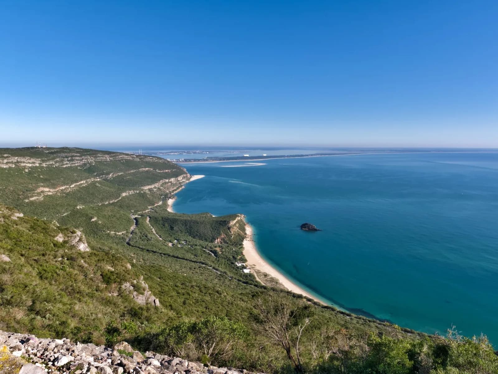 Versants verts de la Serra da Arrábida plongeant vers une plage et une mer turquoise, la péninsule de Tróia à l'horizon