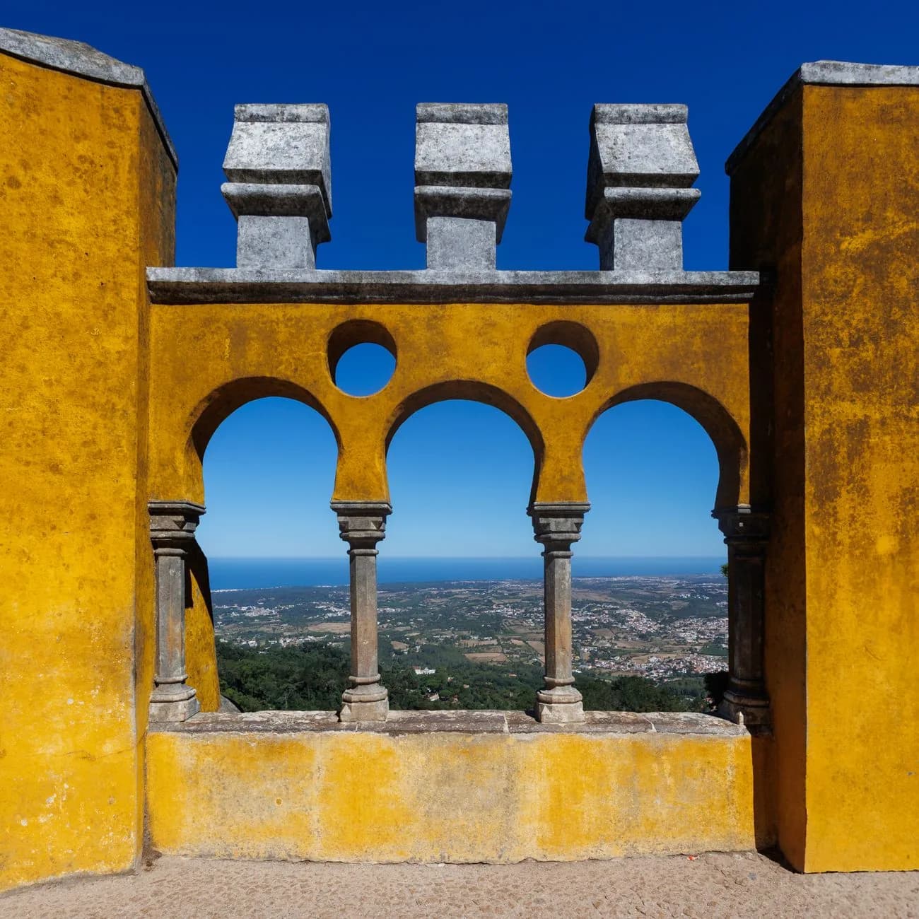 Terrasse aux murs jaunes du palais de Pena, avec trois arcades ouvertes sur la plaine de Sintra et l'océan au loin