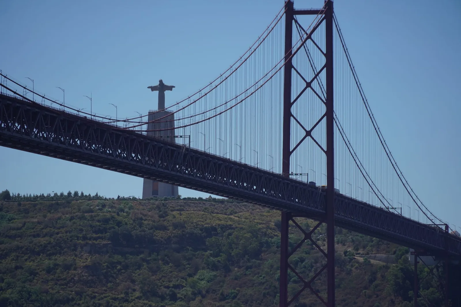 Le Cristo Rei d'Almada dominant la rive sud du Tage, derrière le tablier et un pylône rouge du pont du 25-Avril