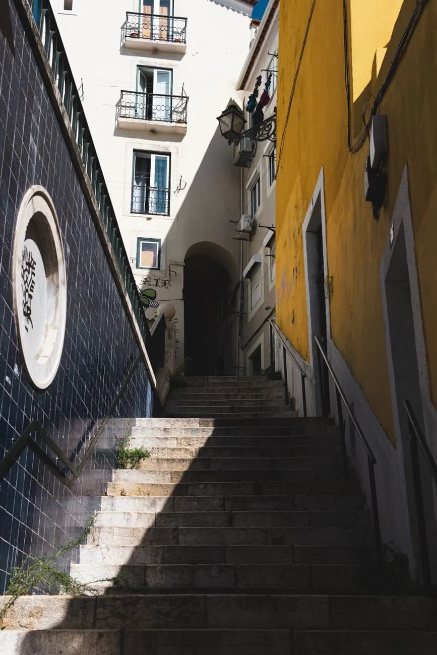 Escalier étroit en pierre entre un mur d'azulejos bleus et une façade jaune, dans la Mouraria à Lisbonne