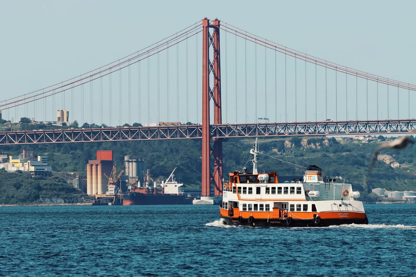 Un ferry de passagers blanc et orange (cacilheiro) traversant le Tage devant le pont du 25-Avril