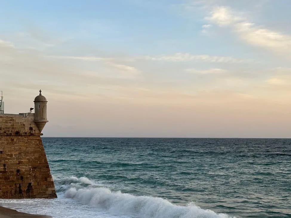 Fort côtier en pierre avec sa guérite, au bord d'une plage de sable où déferlent les vagues
