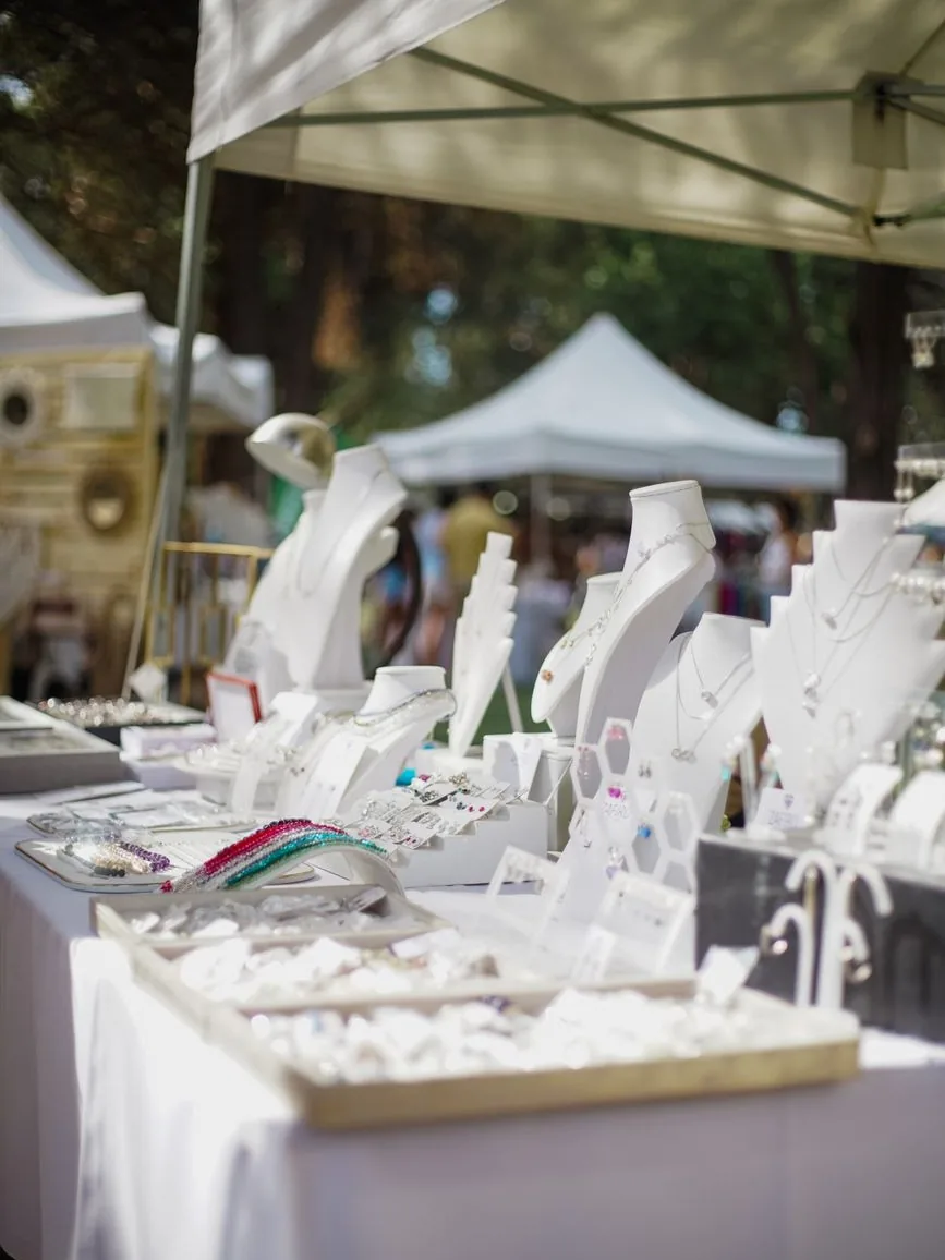 Stand de bijoux faits main sur un marché de créateurs, colliers et bracelets sur présentoirs blancs