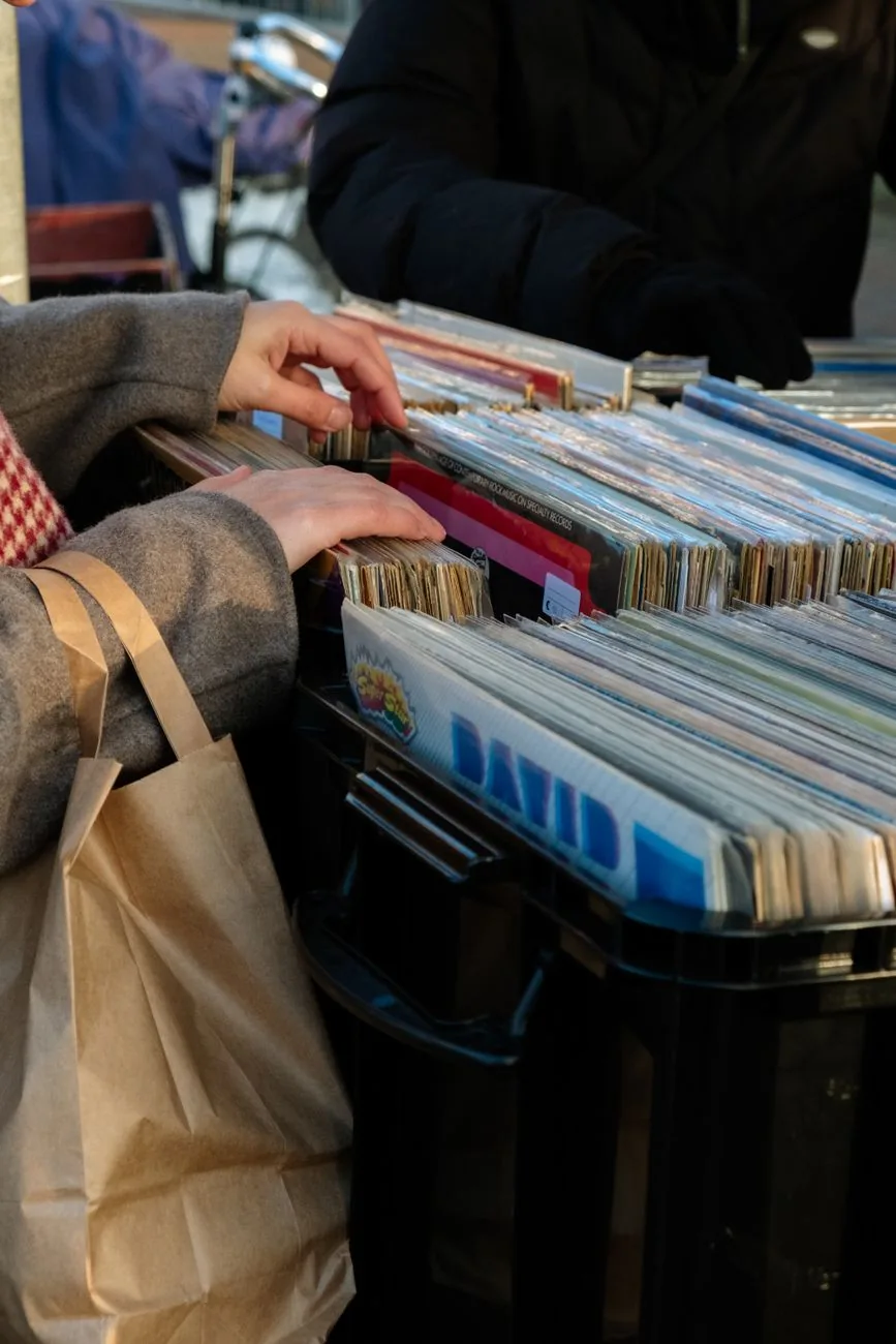 Mains fouillant des bacs de vinyles d'occasion sur un stand de marché