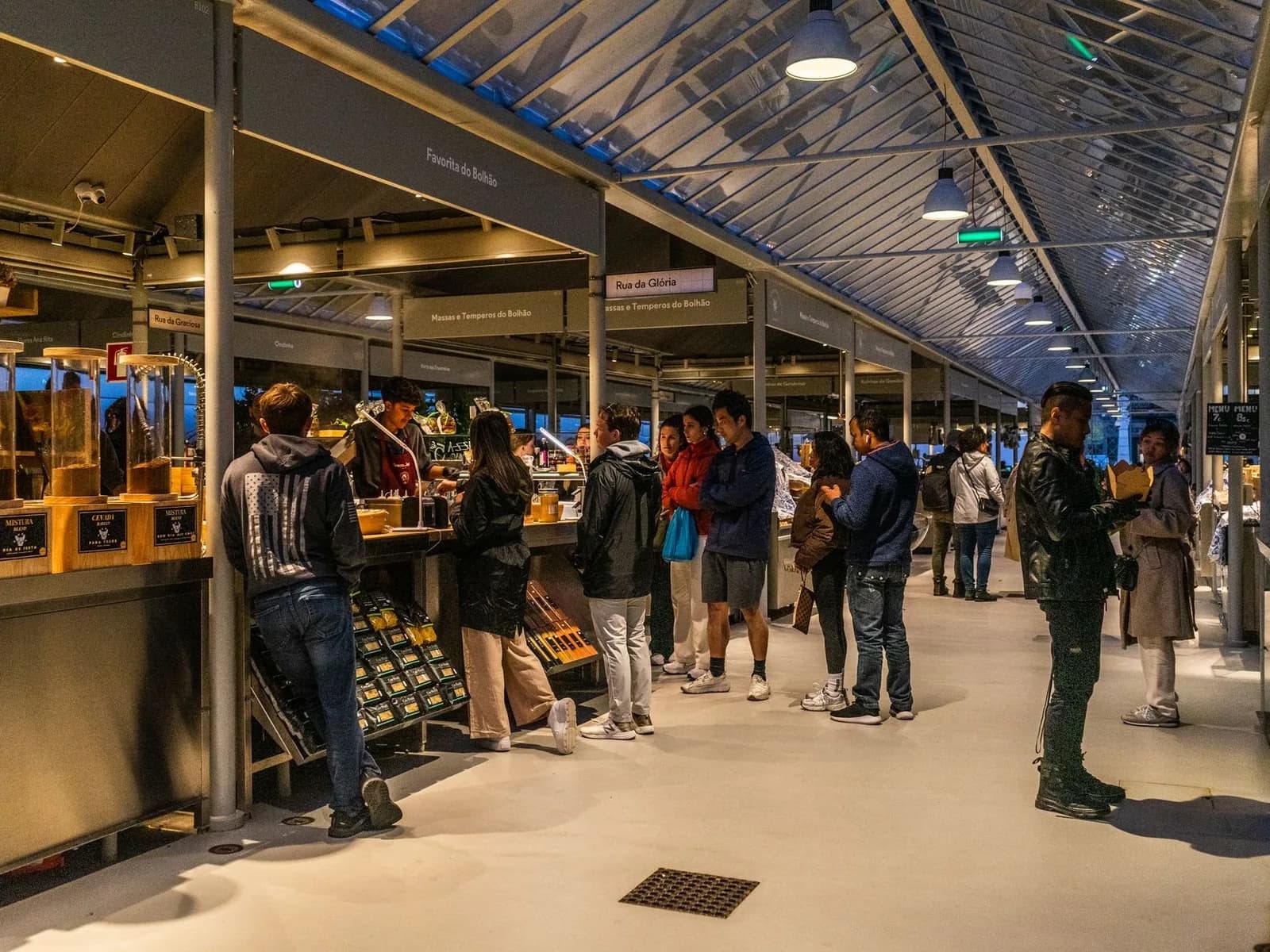 Clients devant les stands d'un marché couvert à Lisbonne, sous une verrière