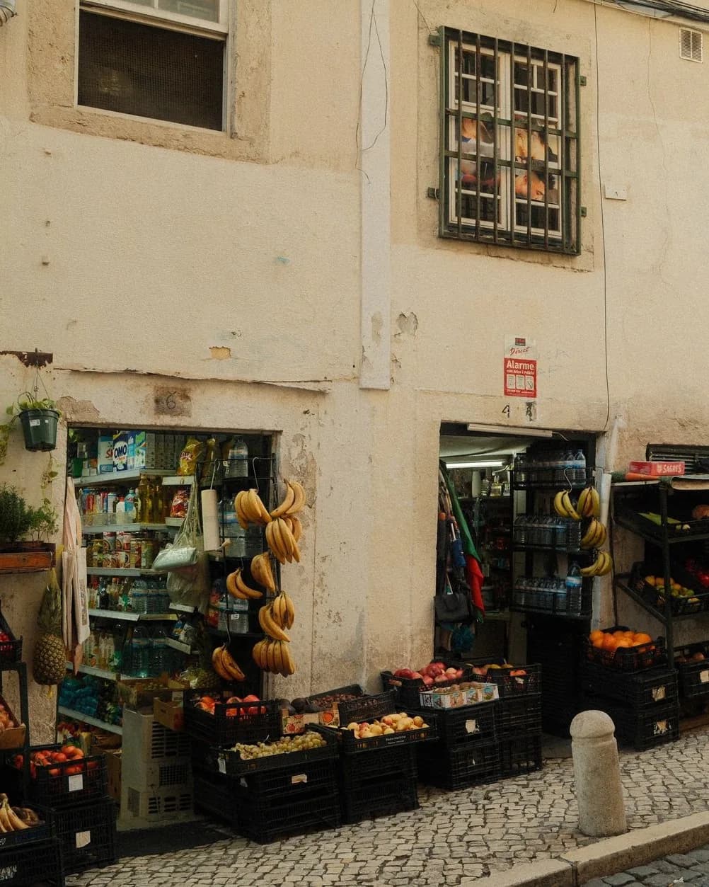 Petite épicerie de quartier à Lisbonne avec bananes suspendues et cageots de fruits sur le trottoir pavé