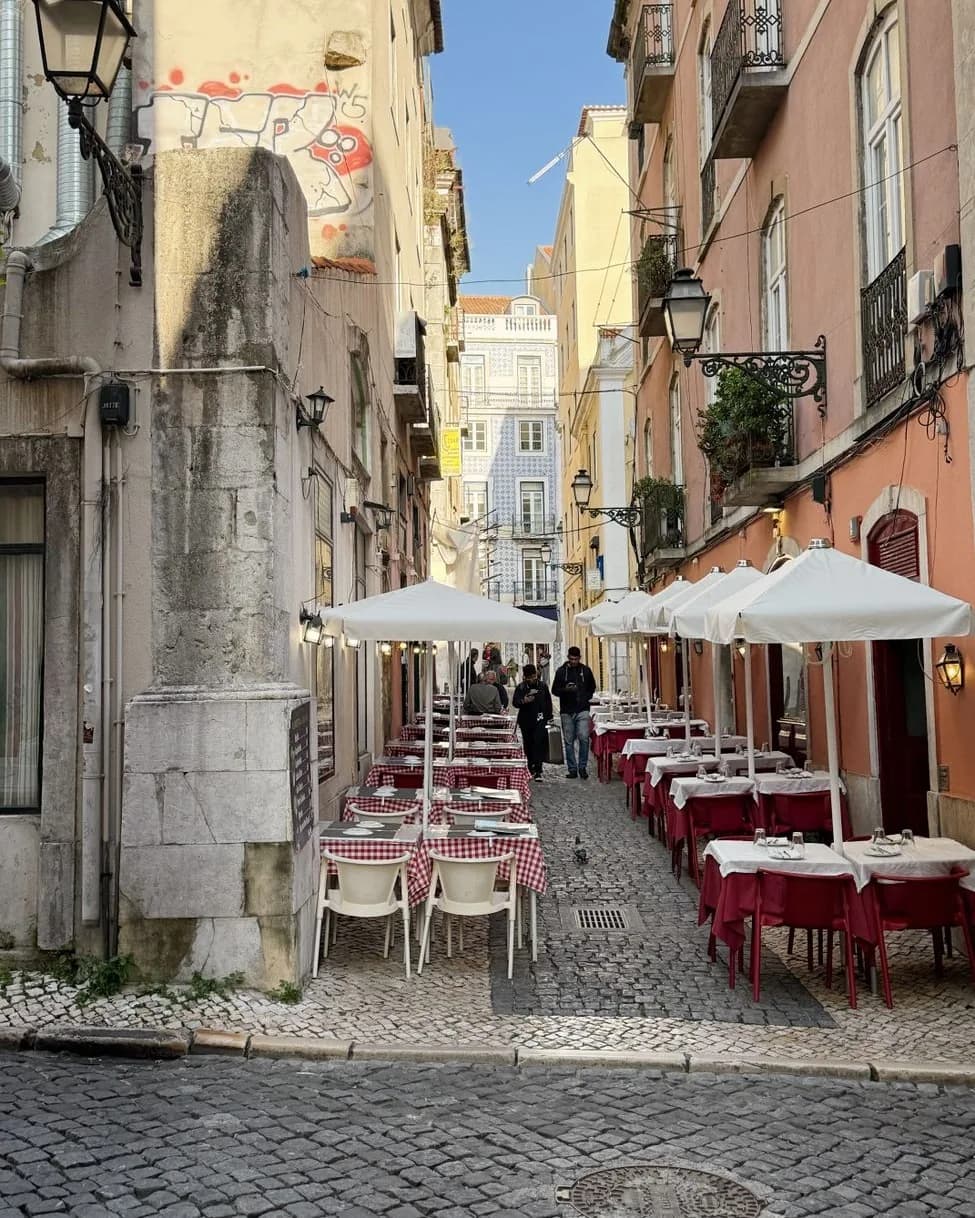 Terrasse de restaurant dans une ruelle pavée de Lisbonne, tables dressées avec nappes à carreaux rouges