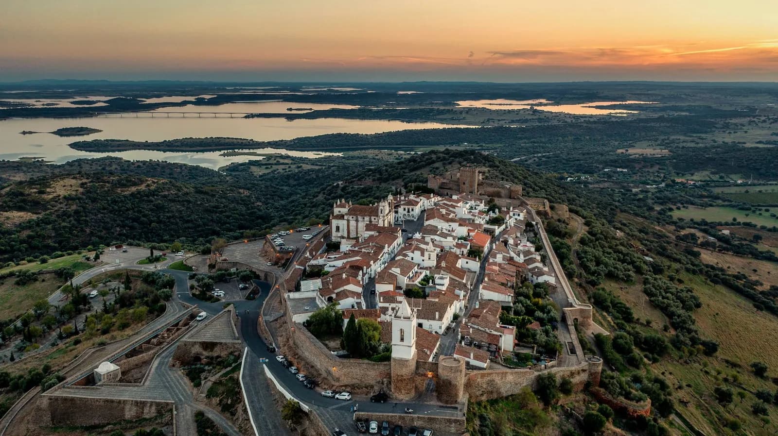 Village fortifié de Monsaraz perché sur sa colline, avec le lac d'Alqueva au loin au coucher du soleil