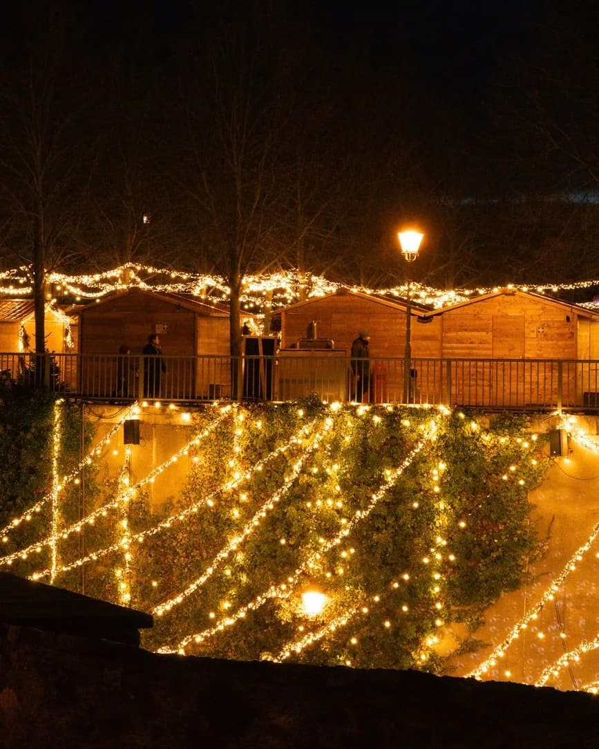 Chalets en bois d'un marché de Noël la nuit, sous des guirlandes lumineuses