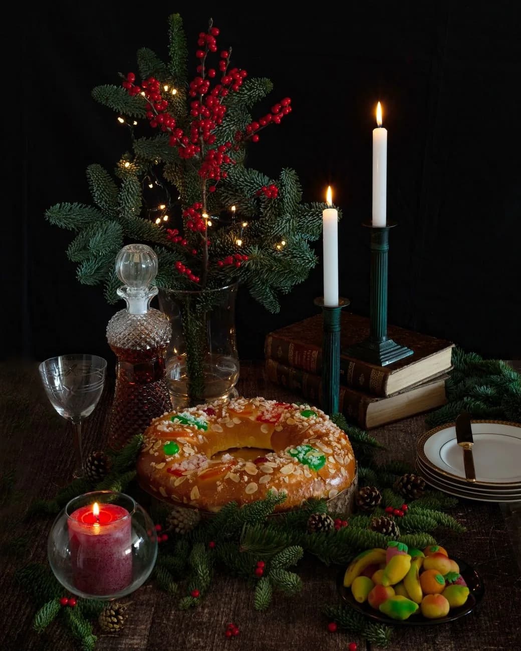 Bolo rei, couronne briochée aux amandes et fruits confits, sur une table de Noël avec branches de sapin et bougies