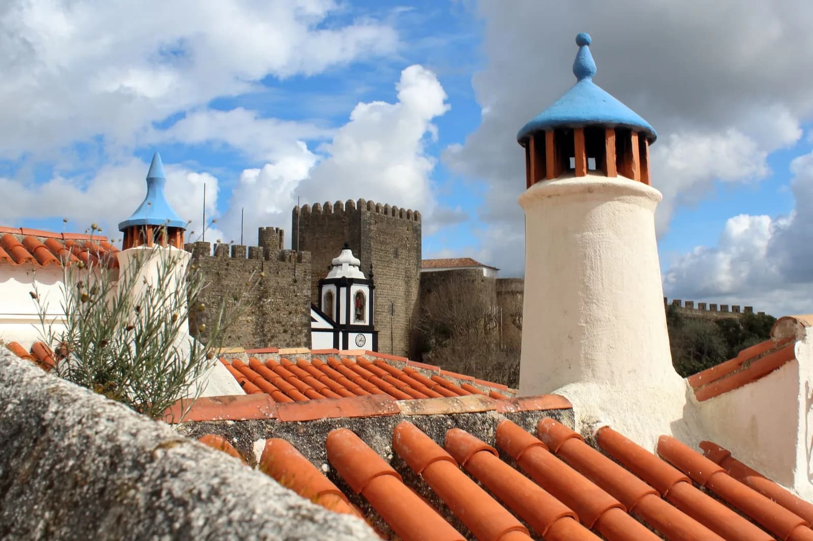 Cheminées blanches à chapeau bleu et toits de tuiles d'Óbidos, avec les remparts du château en fond