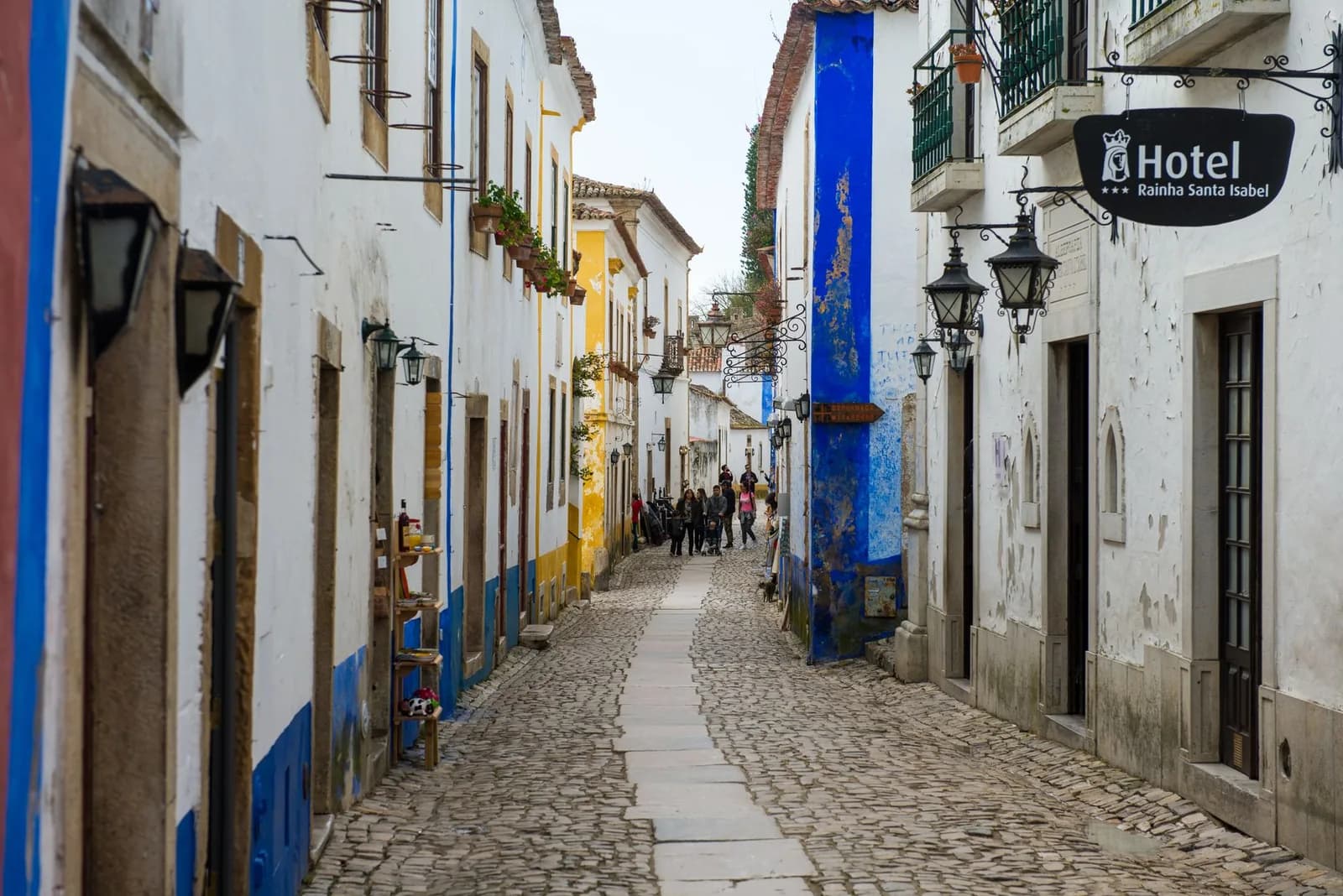 Rue pavée d'Óbidos bordée de maisons blanches à liserés bleus et jaunes