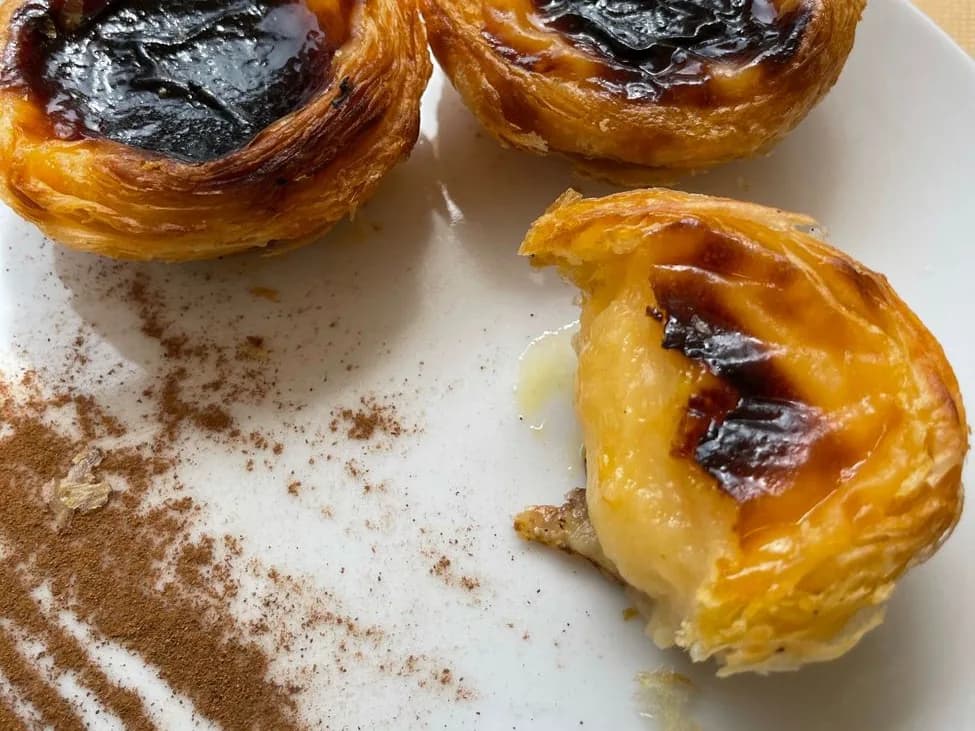 Pastéis de nata dorés saupoudrés de cannelle, dont un entamé qui laisse voir la crème