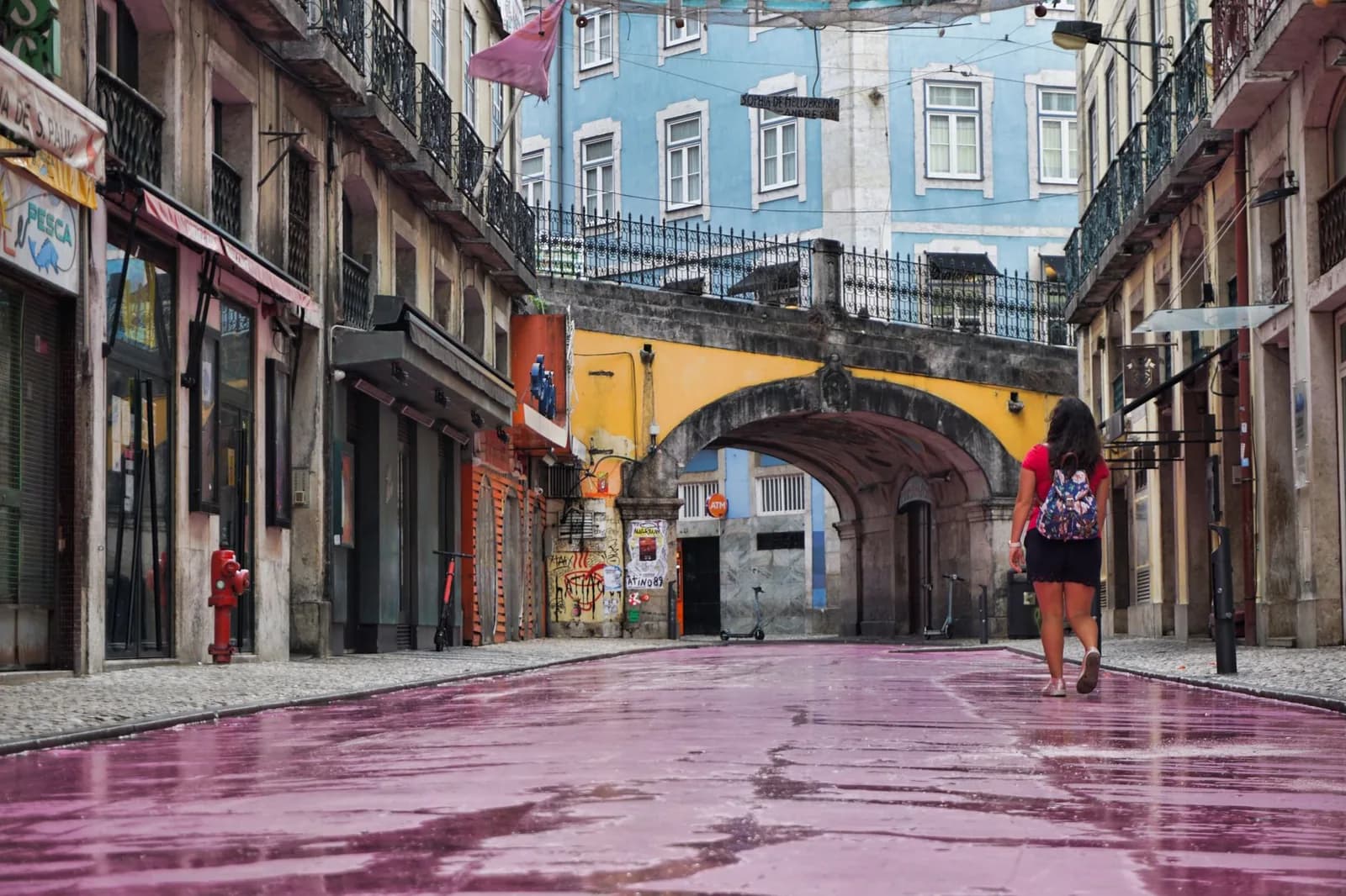 Le sol rose de la Pink Street (Rua Nova do Carvalho) à Cais do Sodré, avec un passant et un passage voûté, Lisbonne