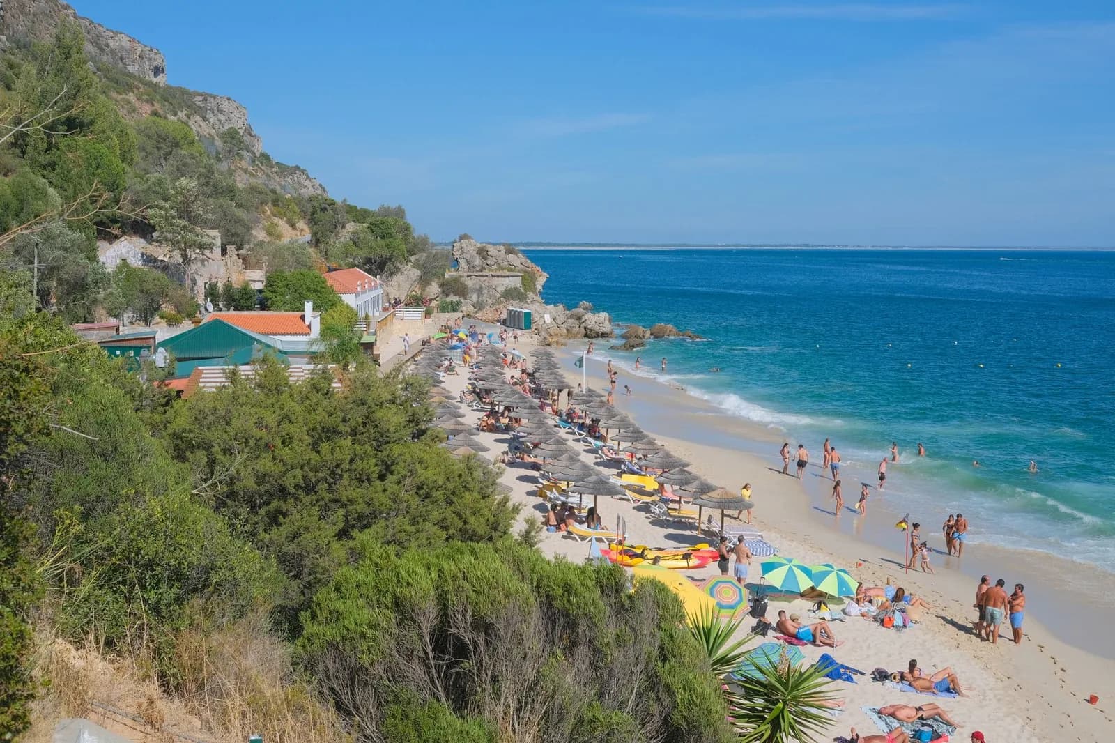 Plage de sable et parasols au pied de collines boisées de l'Arrábida