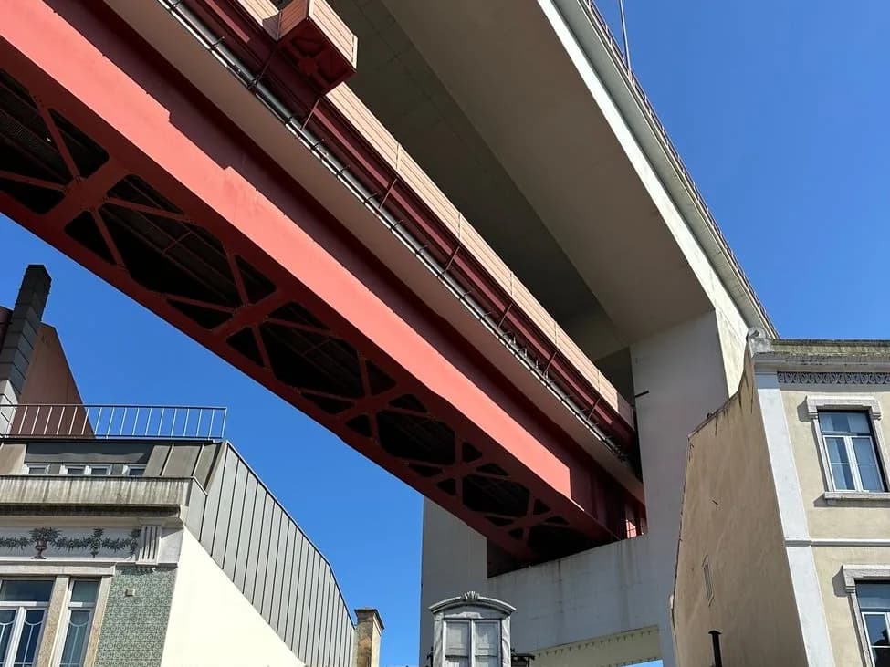Tablier métallique rouge du pont du 25-Avril vu d'en dessous, au-dessus des maisons d'Alcântara, Lisbonne
