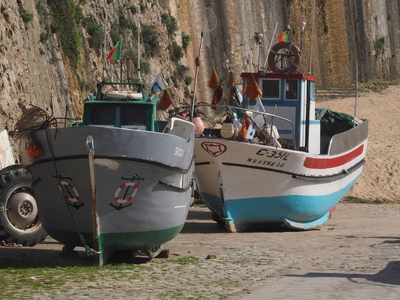 Bateaux de pêche portugais tirés au sec sur un quai de sable, au pied d'une falaise