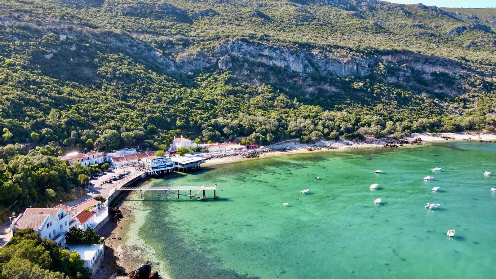 Baie turquoise du Portinho da Arrábida, ses bateaux au mouillage et ses maisons au pied de la montagne