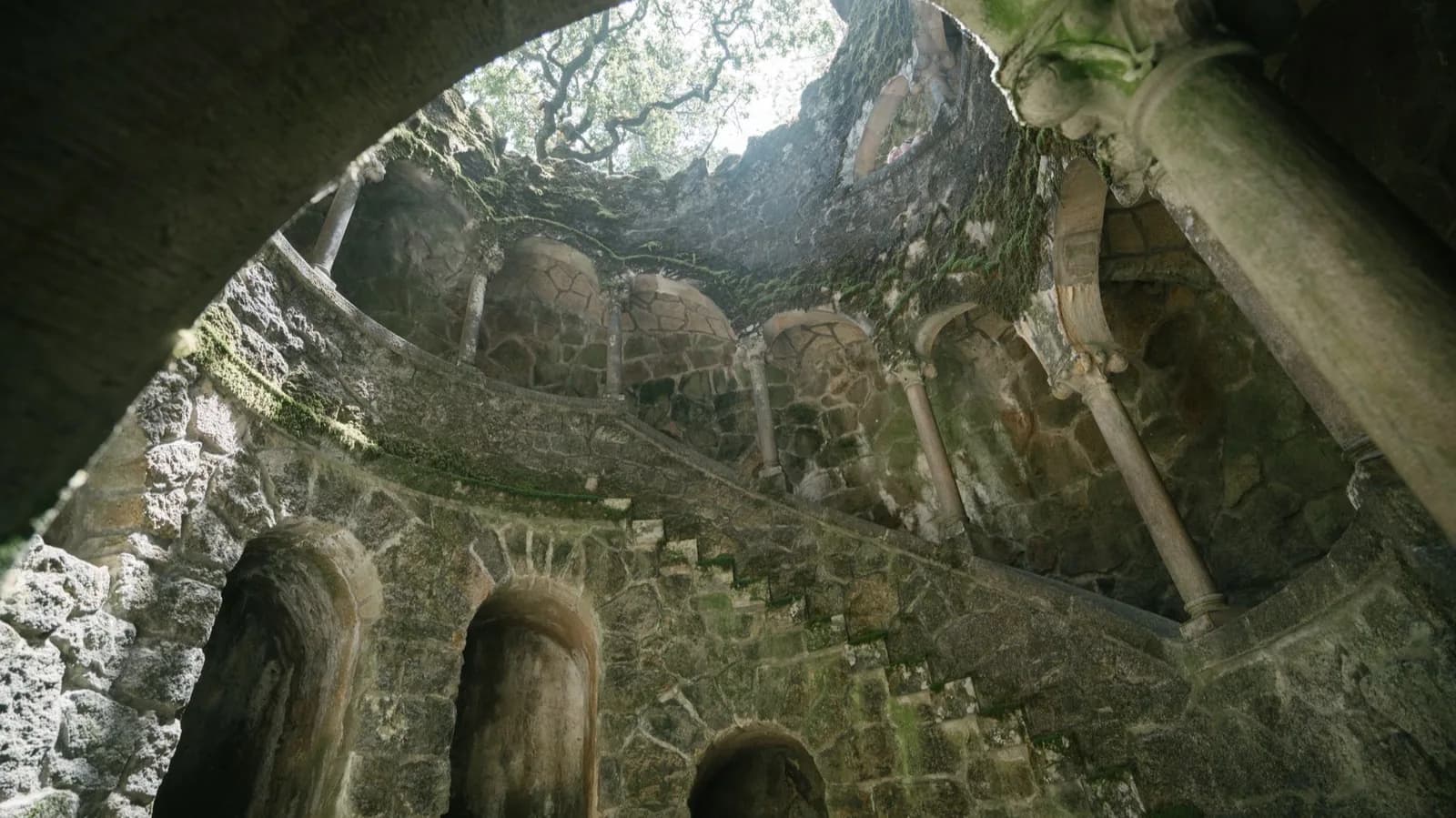 Le puits initiatique de la Quinta da Regaleira à Sintra, vu d'en bas, avec ses escaliers en spirale et ses arches ouvertes vers le ciel