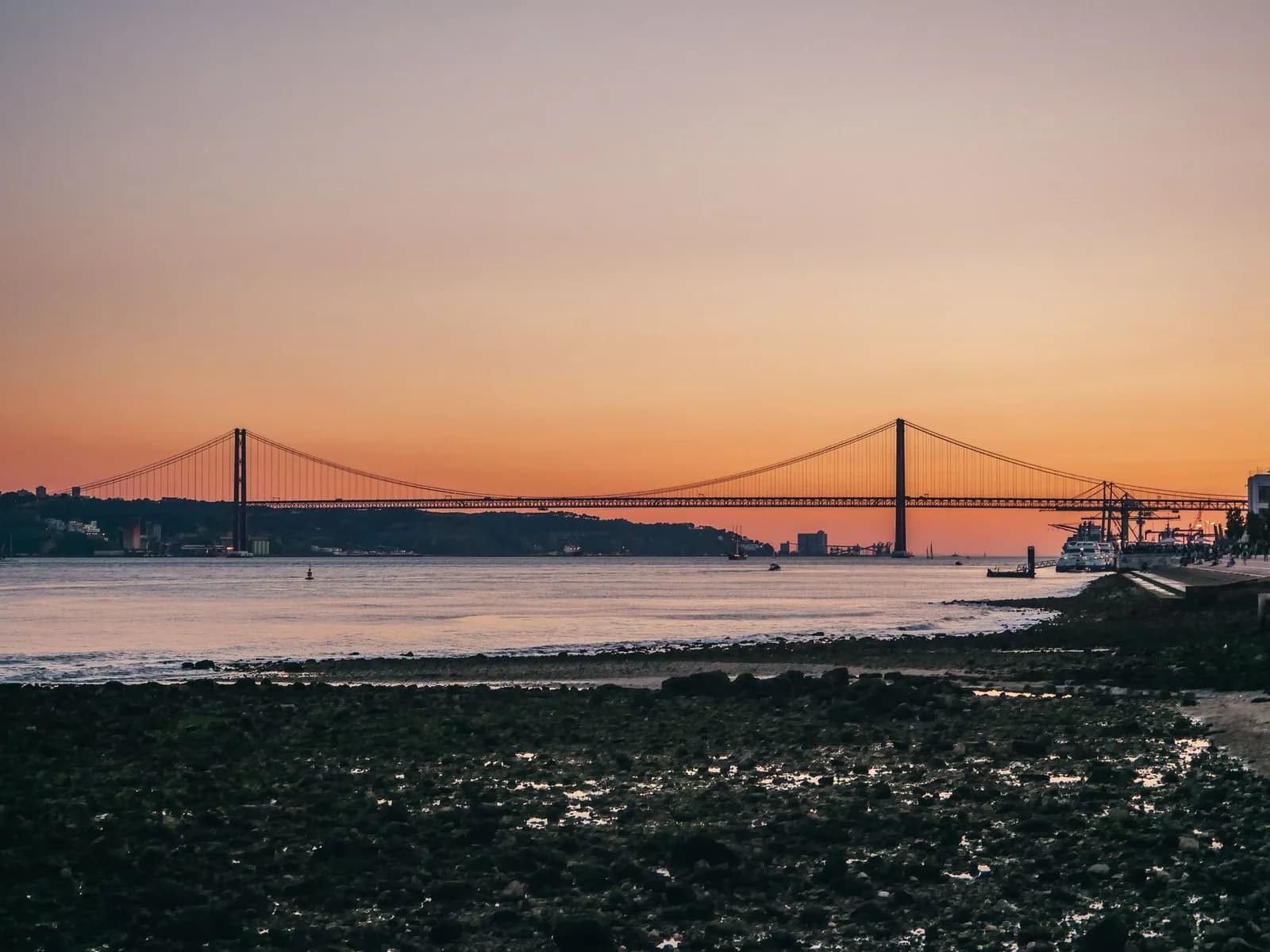 Coucher de soleil orangé sur le Tage depuis les quais de Lisbonne, avec le pont du 25-Avril en silhouette