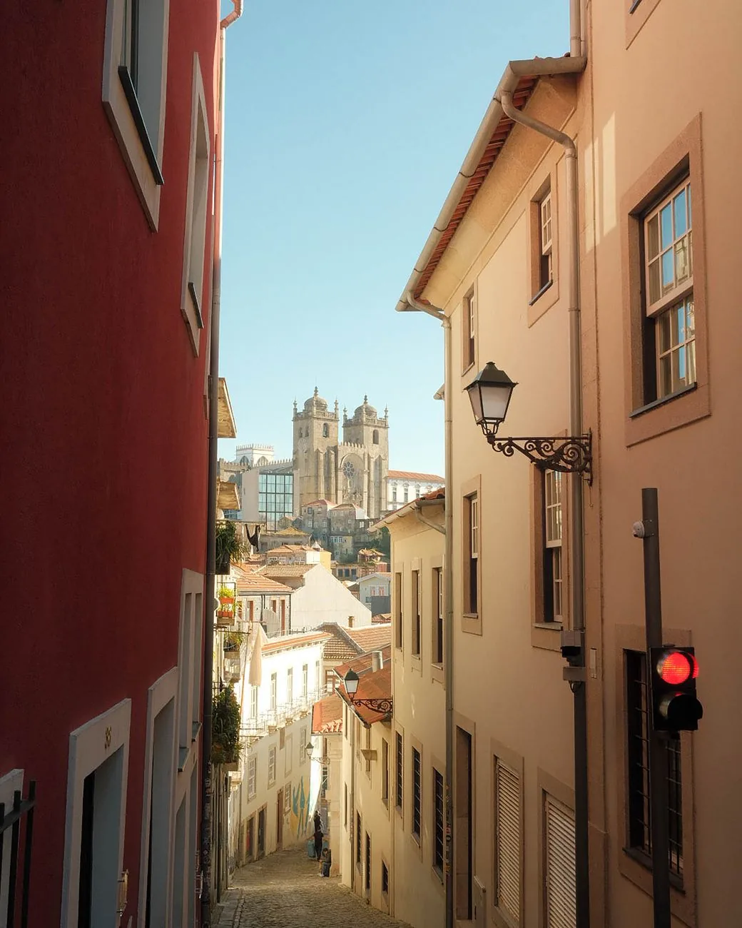 Rue en pente de l'Alfama entre façades rouge et rose, avec la cathédrale Sé au fond, Lisbonne