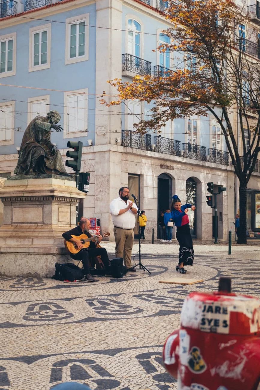 Statue en bronze et musiciens de rue sur une place pavée du Chiado, façades bleues et ocre, Lisbonne