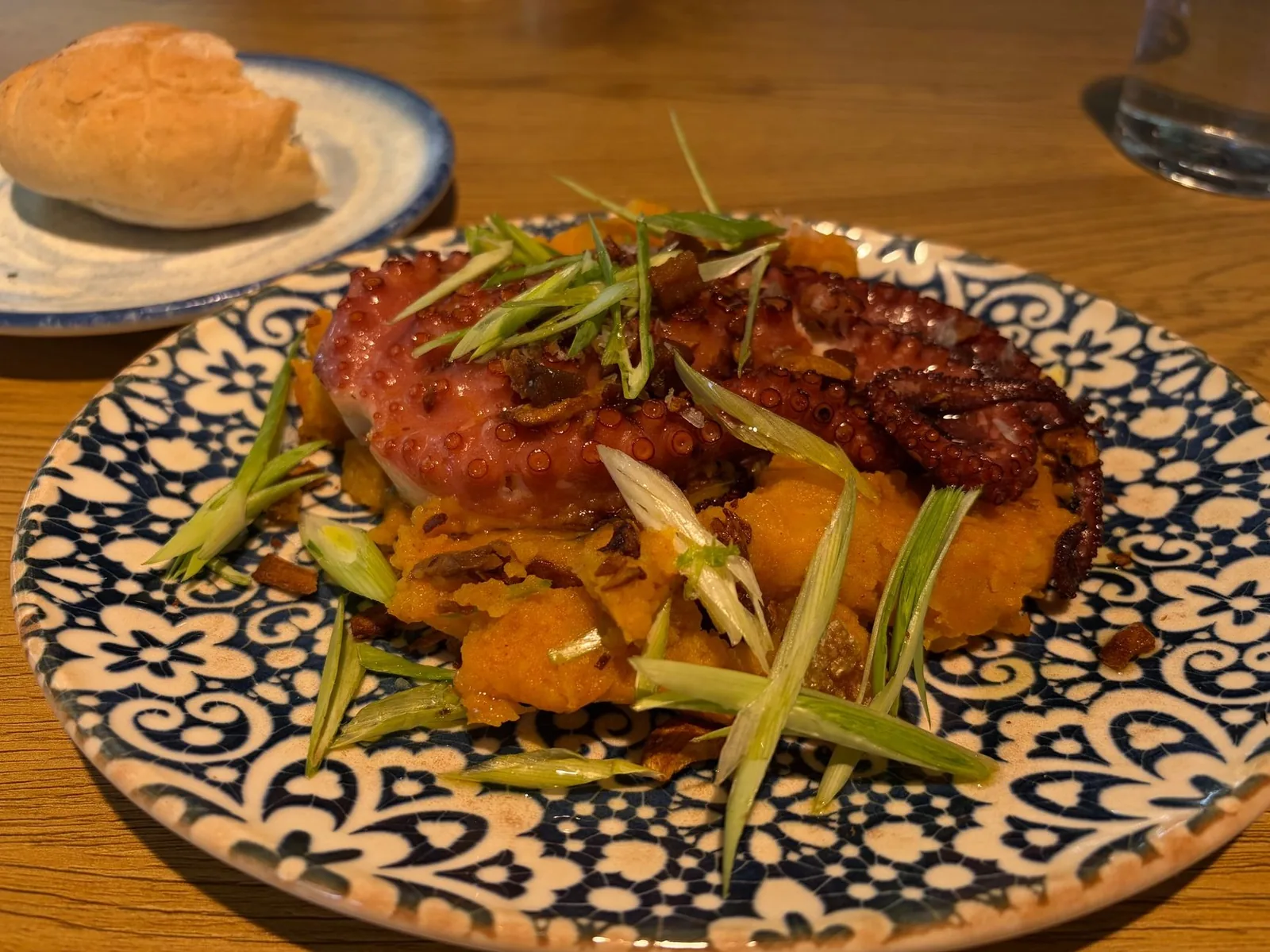Poulpe grillé servi sur purée de patate douce dans une assiette en céramique