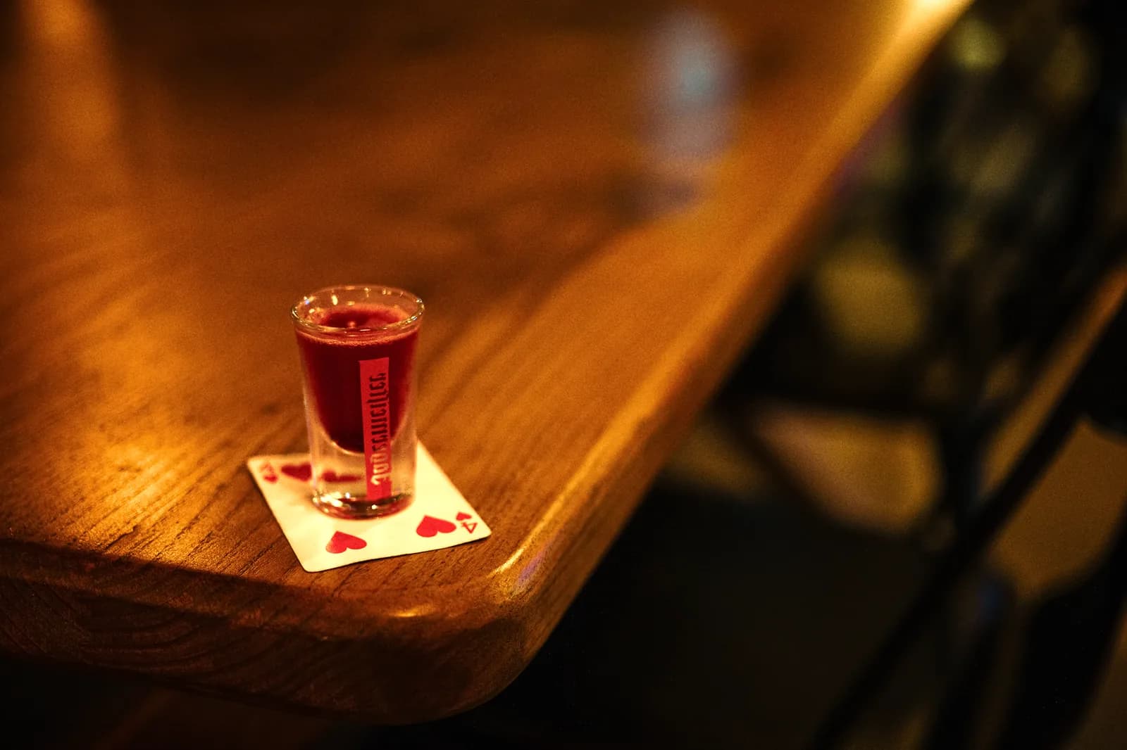 Petit verre de liqueur rouge posé sur un comptoir en bois